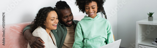 Φωτογραφία happy african american family watching comedy movie on laptop in living room, banner