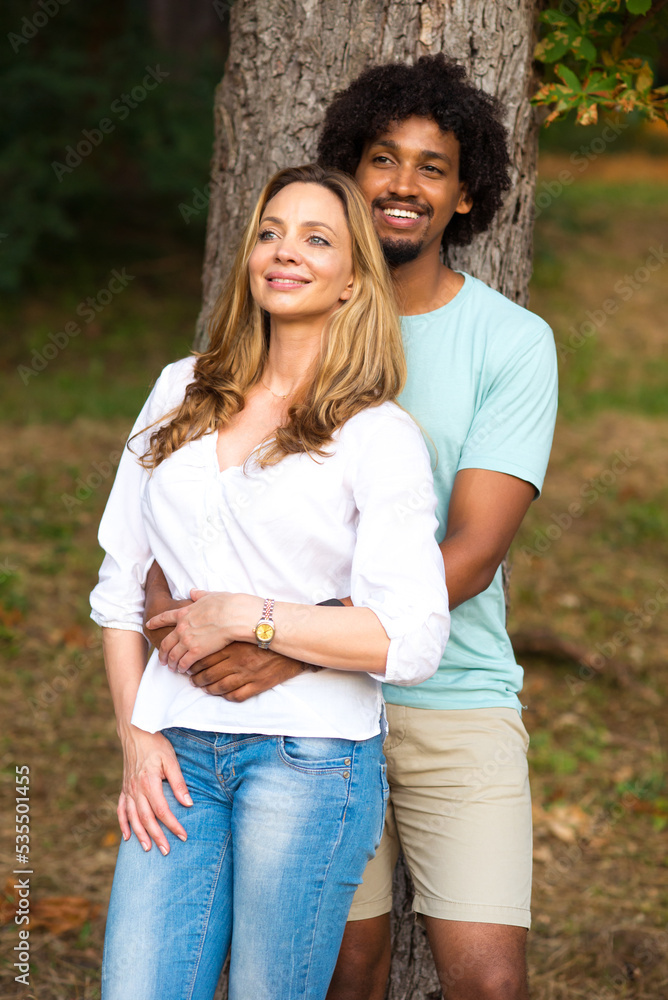 Young smiling mixed race couple standing and hugging in the nature on a beautiful summer day Young smiling mixed race couple standing and hugging in the nature on a beautiful summer day