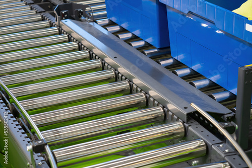 Production line fragment. Steel spinning rollers close-up. Production line and blue containers. Production line for factory industry. Modern industrial equipment. Factory conveyor belt. photo