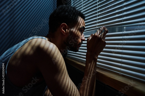 Foto Side view view of young sleepless man looking through venetian blinds on window