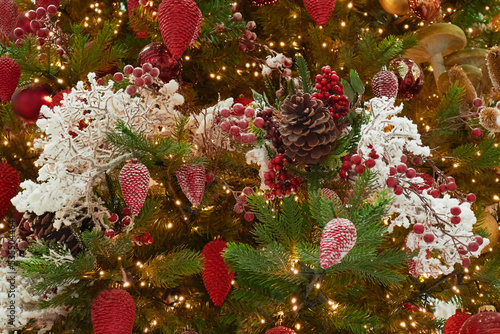 Decorative red berries and cones on a Christmas tree with festive lights.