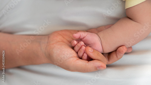 Mother holding baby hand and showing finger and fingernail on white sheet bed