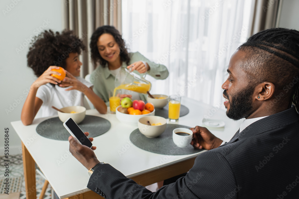 african american man in suit using smartphone with blank screen during breakfast with family on blurred background. african american man in suit using smartphone with blank screen during breakfast with family on blurred background.