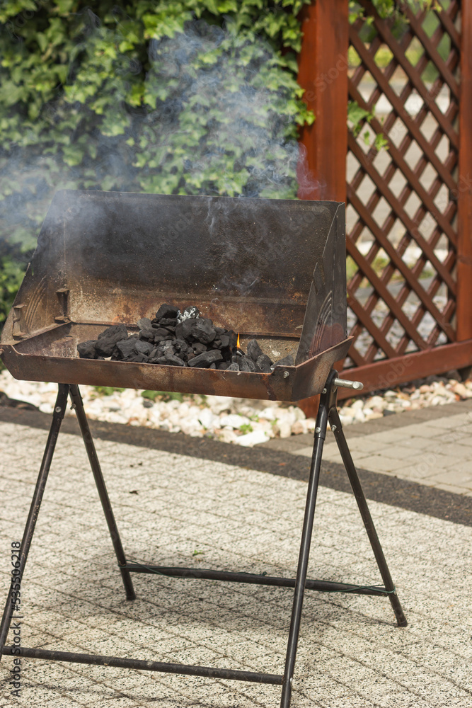 Smoke over flaming pile of charcoal in metal brazier on backyard. Folding portable brazier filled with burning coal. Smoke over flaming pile of charcoal in metal brazier on backyard. Folding portable brazier filled with burning coal.