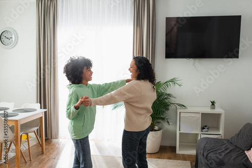 cheerful african american woman holding hands while dancing with preteen daughter.