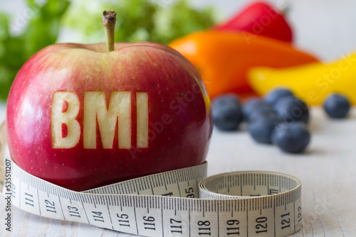 Red apple with text BMI and measuring tape on background of vegetables and fruits, diet and healthy weight concept photo
