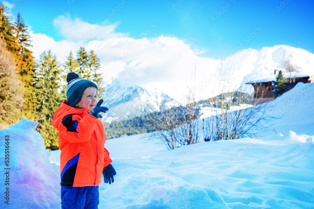 Happy toddler boy pointing at something in snowy mountains