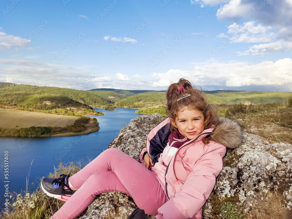 Cute Toddler Girl sitting on a rocks high above a lake with stunning mountain view . Kid in the nature Cute Toddler Girl sitting on a rocks high above a lake with stunning mountain view . Kid in the nature