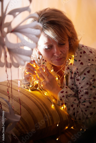 Happy adult middle aged woman wearing pajamas in room with Christmas decorations. New Year holiday in Russia