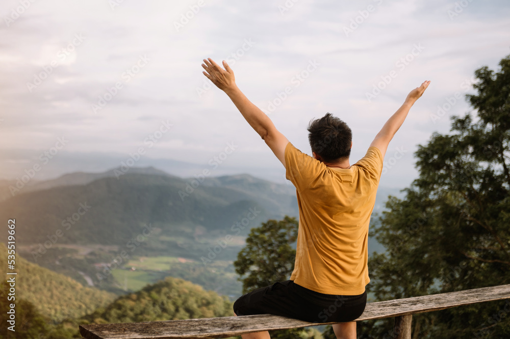 Rear view image of a male traveler sitting and looking at a beautiful mountain,sky field and nature view Rear view image of a male traveler sitting and looking at a beautiful mountain,sky field and nature view