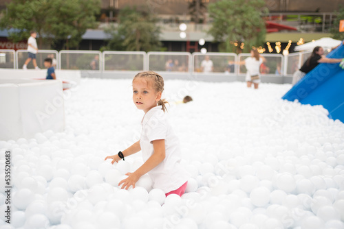 Happy little girl playing white plastic balls pool in amusement park. playground for kids. photo