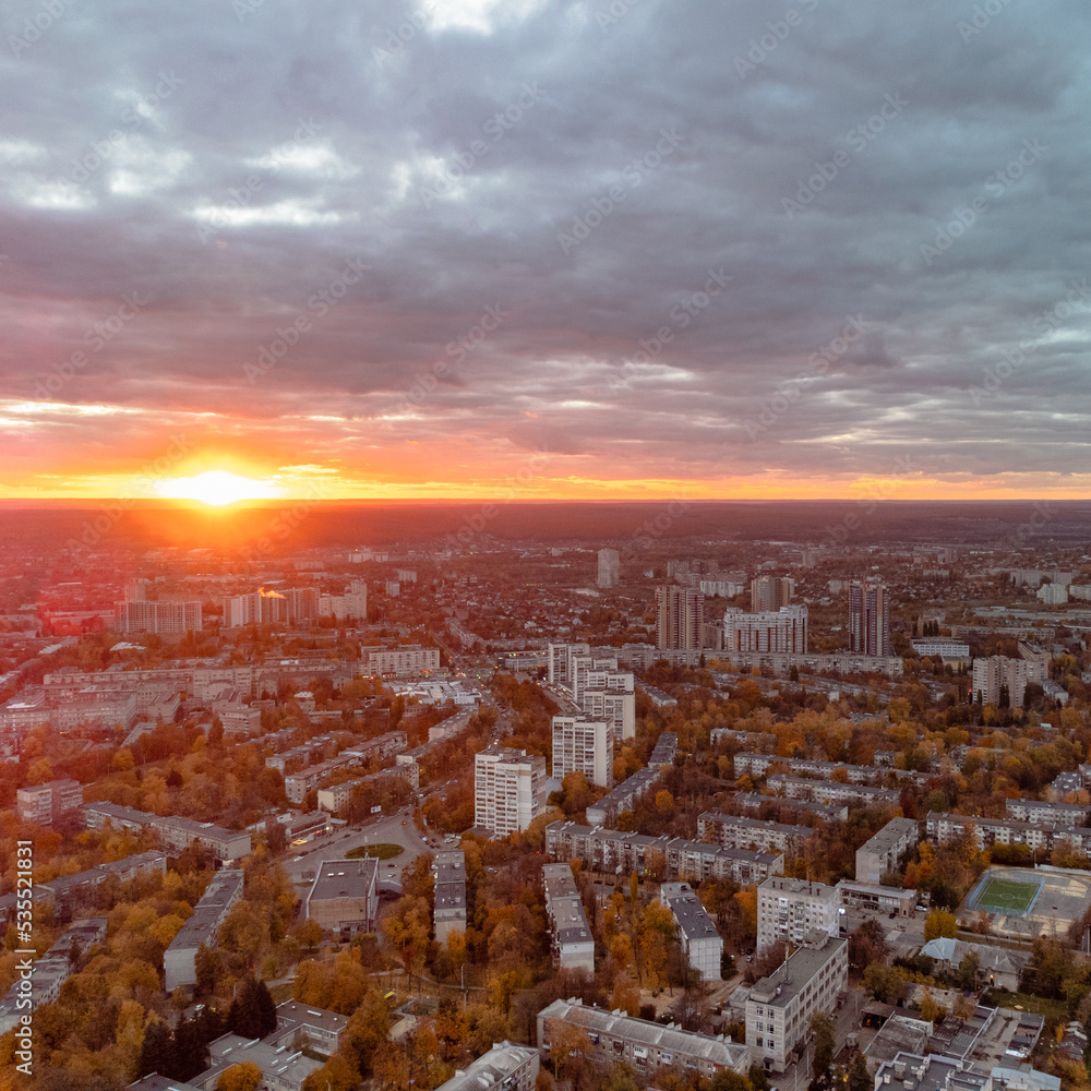 Aerial vivid autumn city sunset view with sun shine in gray clouds. Residential district buildings in evening light. Kharkiv, Ukraine