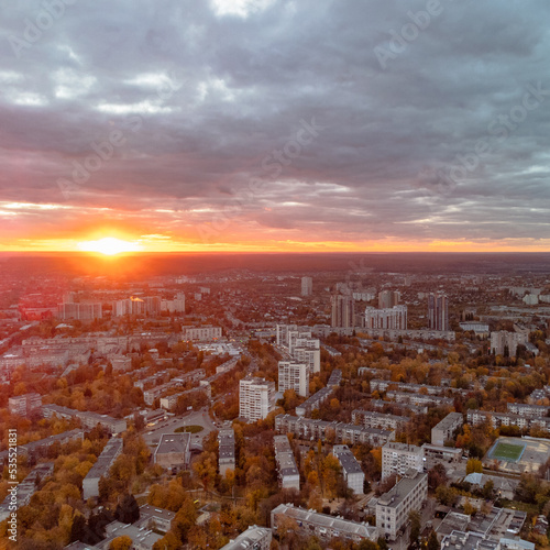 Aerial vivid autumn city sunset view with sun shine in gray clouds. Residential district buildings in evening light. Kharkiv, Ukraine