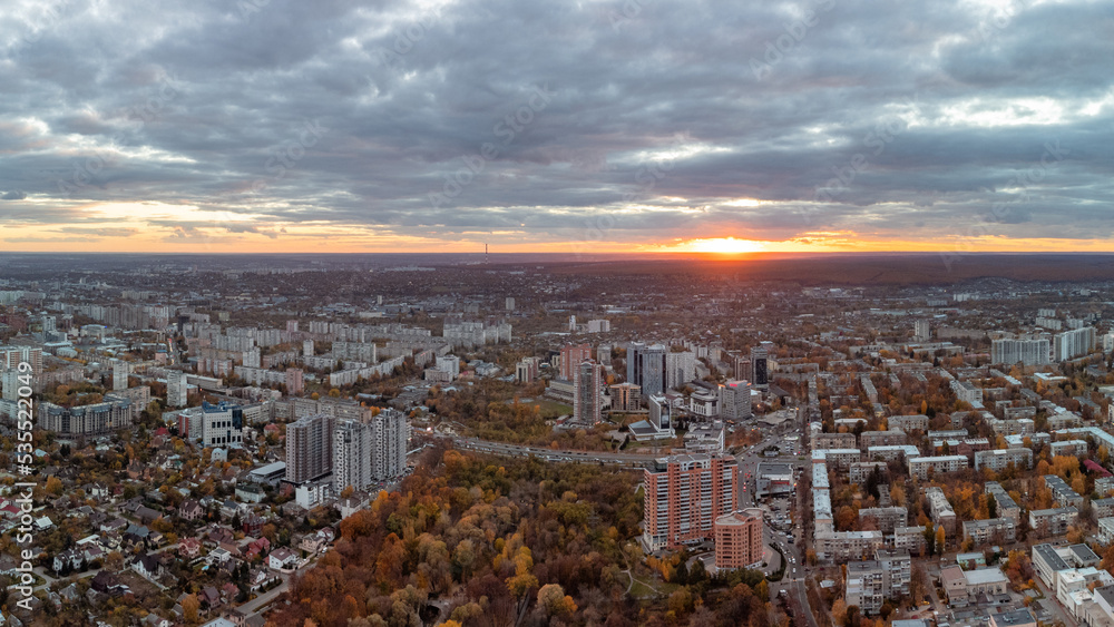 Aerial vivid autumn city park sunset panorama view with epic cloudscape. Botanical garden and Kharkiv city center. Residential district buildings and cars driving in evening