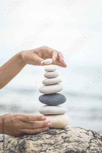 Canvas Print Tanned woman hands stacked pebble stones tower on sea beach relaxing harmony sum