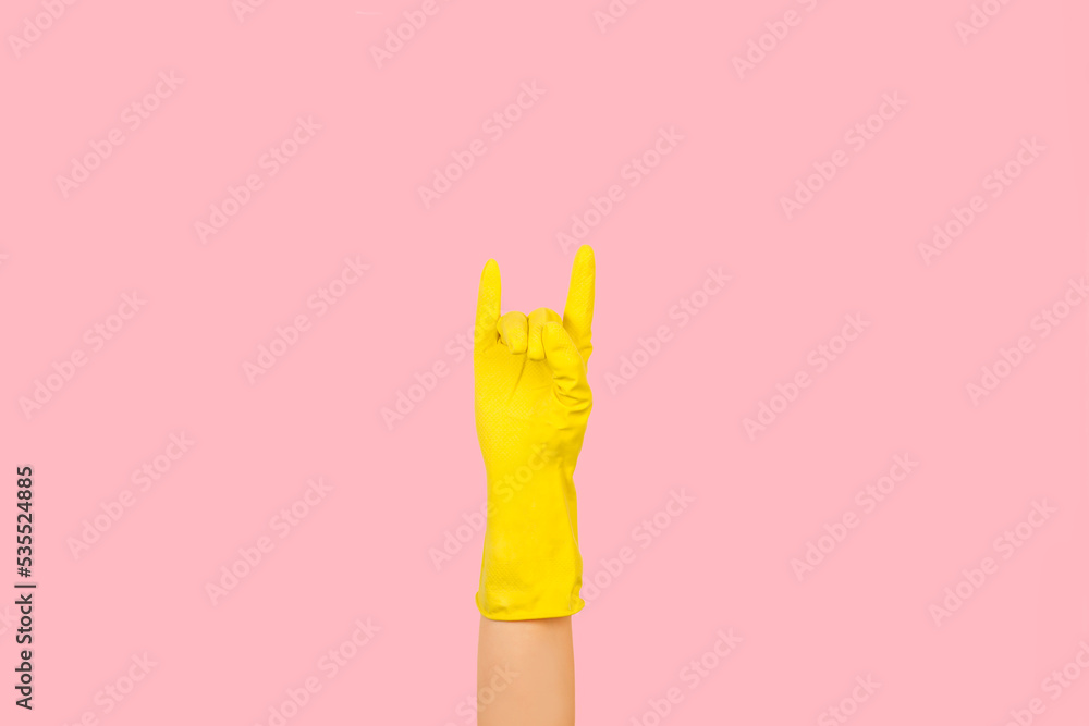 Obraz premium Mano con guante de látex amarillo mostrando el gesto de rock'n'roll sobre un fondo rosa pastel. Vista de frente y de cerca. Copy space