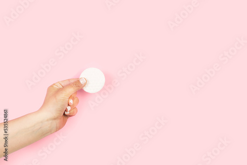 Mano de mujer sosteniendo un disco de algodón sobre un fondo rosa pastel. Vista de frente y de cerca. Copy space
