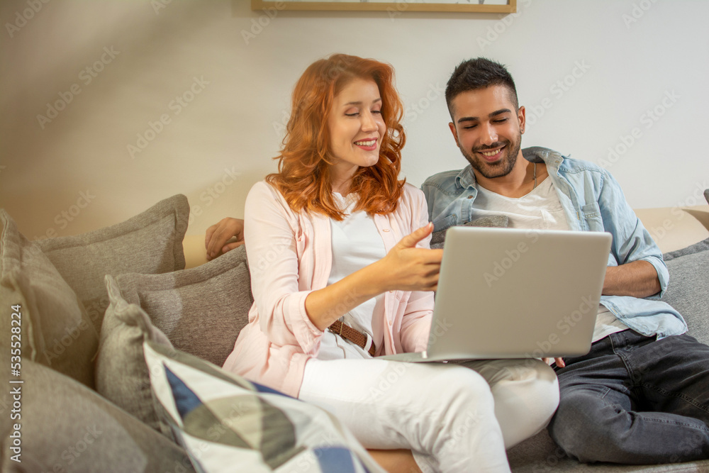 Cute happy couple using laptop while sitting on sofa at home.