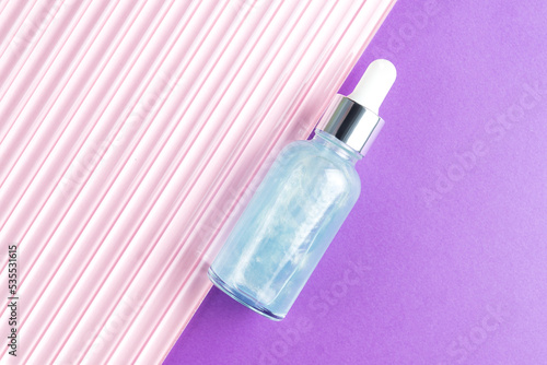 Beauty face oil in blue glass dropper bottle om pink and purple background. Trendy shoot of cosmetics packaging. Essential oil with natural ingredients. Cruelty free cosmetics