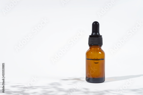 Amber bottle with black cap with beauty serum or essential oil with flowers shadows. White background with daylight. Beauty concept for face and body care. Soothing cbd oil