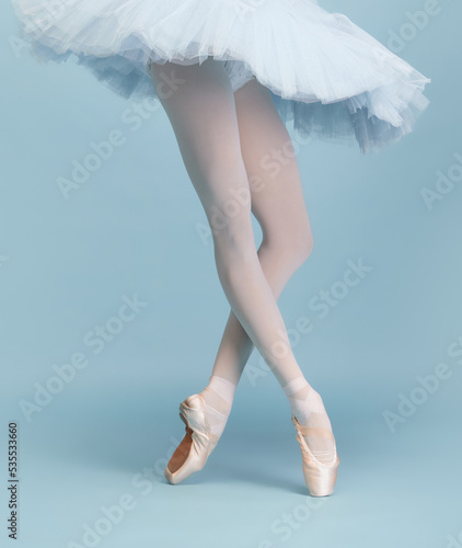 Cropped image of female legs, ballerina in tutu and pointe standing on tiptoe isolated isolated over blue studio background