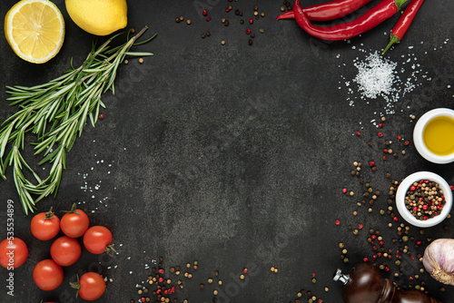 Food cooking background on dark stone table. Top view of olive oil, cherry tomato, herbs and spices on rustic black slate. Colorful food ingredients border.