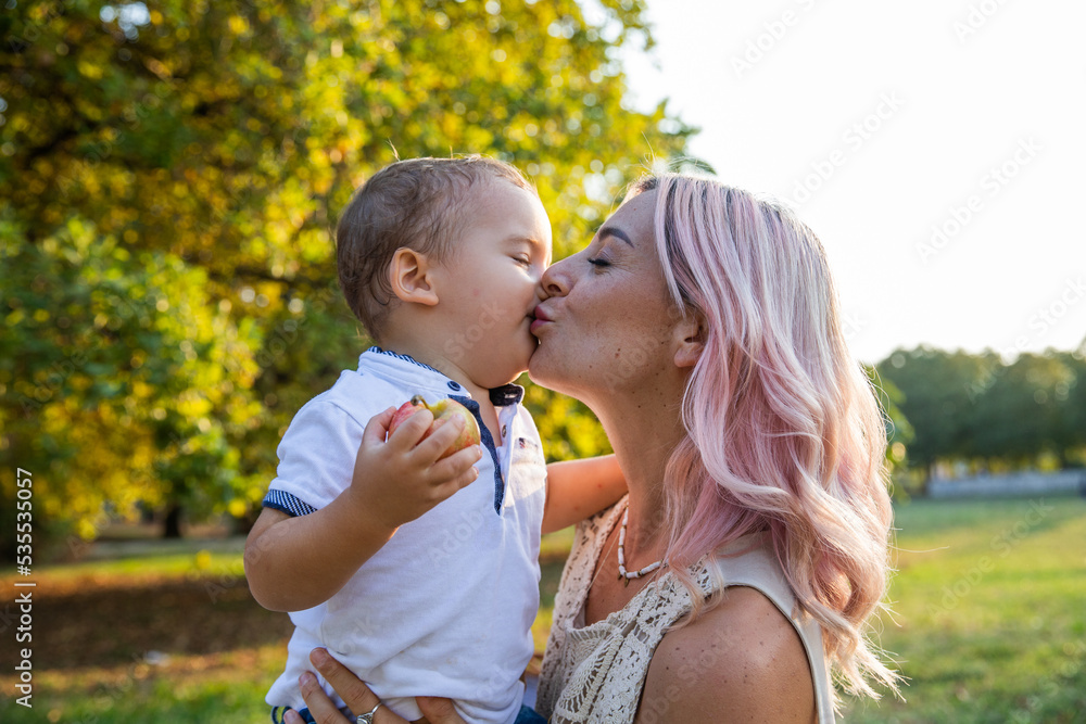 Mother tenderly kisses her baby on the mouth during a walk in the park Mother tenderly kisses her baby on the mouth during a walk in the park