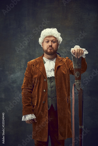Creative portrait of retro style hunter in vintage hunting clothing with old gun isolated over dark background. Art, fashion, emotions, traditions, hobby concept