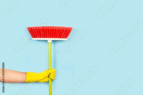Tableau sur toile Mano con guante de látex amarillo sosteniendo una escoba roja sobre un fondo celeste pastel liso y aislado