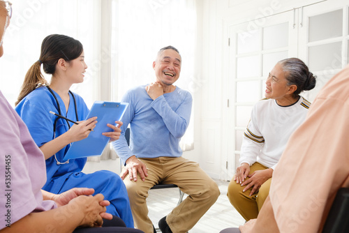 The caregiver therapist sits with a group of Asian senior people in a circle for checking physical and mental health in a group elderly therapy session. The nursing home facilitates a support group