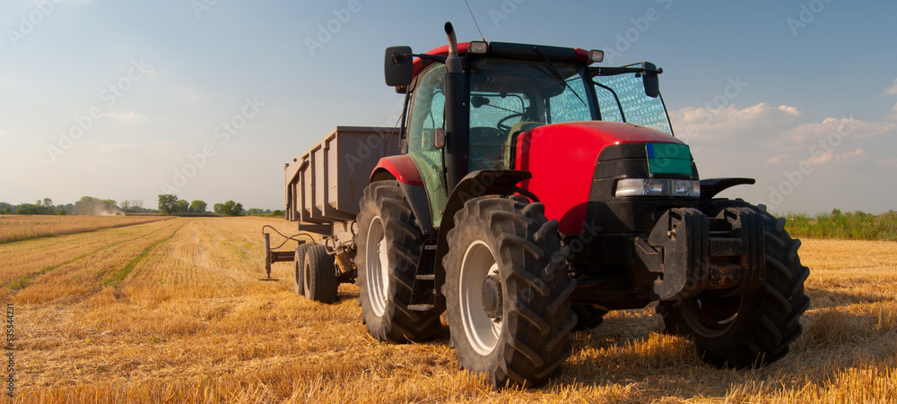 Obraz premium Tractor with a trailer on agricultural field during wheat summer harvest