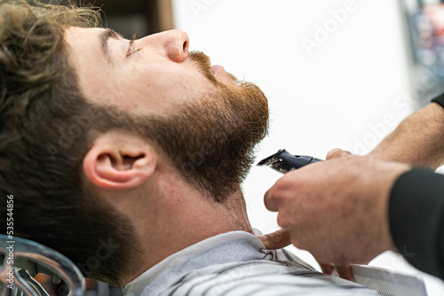 A bearded client of a shaving salon has his beard trimmed with a clipper