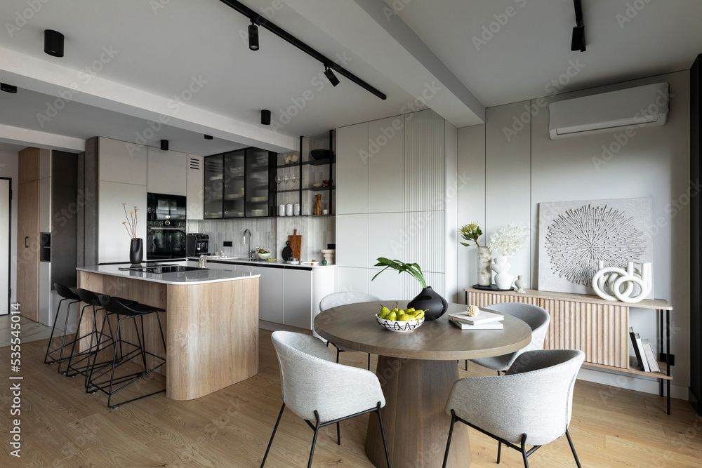 Contemporary design of dining room interior with round table, gray chairs, wooden floor, decorations, flowers in vase, paintings and elegant personal accessories. Stylish home decor. Template. Contemporary design of dining room interior with round table, gray chairs, wooden floor, decorations, flowers in vase, paintings and elegant personal accessories. Stylish home decor. Template.