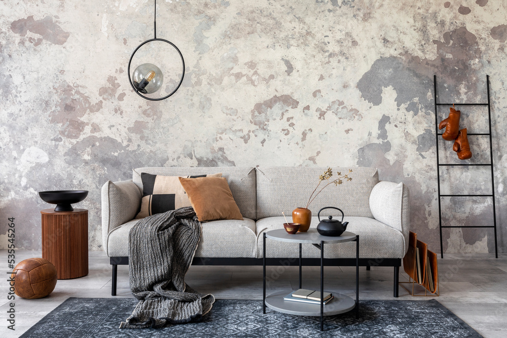 Loft style of modern apartment with grey design sofa, coffee table, side  table, ladder, pedant lamp, carpet, tea pot, decoration and elegant  accessories. Home decor. Concrete grunge wall. Template. Photos | Adobe