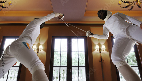 Two female fencing athletes fight in old fencing hall photo