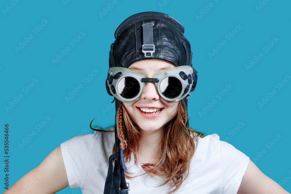 A symbol of travel and development - a teenager dreams of flying. A young girl-pilot against the sky. Girl in an aviator helmet, portrait on a blue background A symbol of travel and development - a teenager dreams of flying. A young girl-pilot against the sky. Girl in an aviator helmet, portrait on a blue background