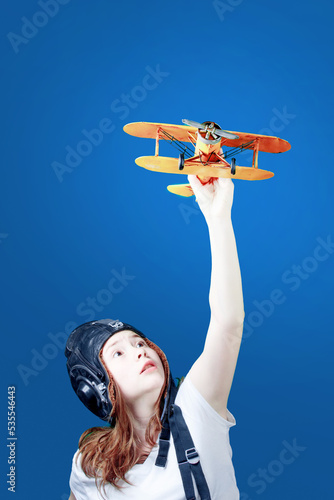 Girl with a toy plane. A symbol of travel and development - a teenager dreams of flying. Young girl-pilot against the blue sky