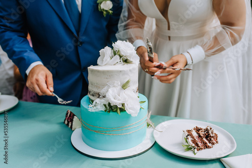 The bride and groom cut a sweet, delicious, sweet wedding cake with a knife, standing on the table, putting it into large pieces close-up on a plate.