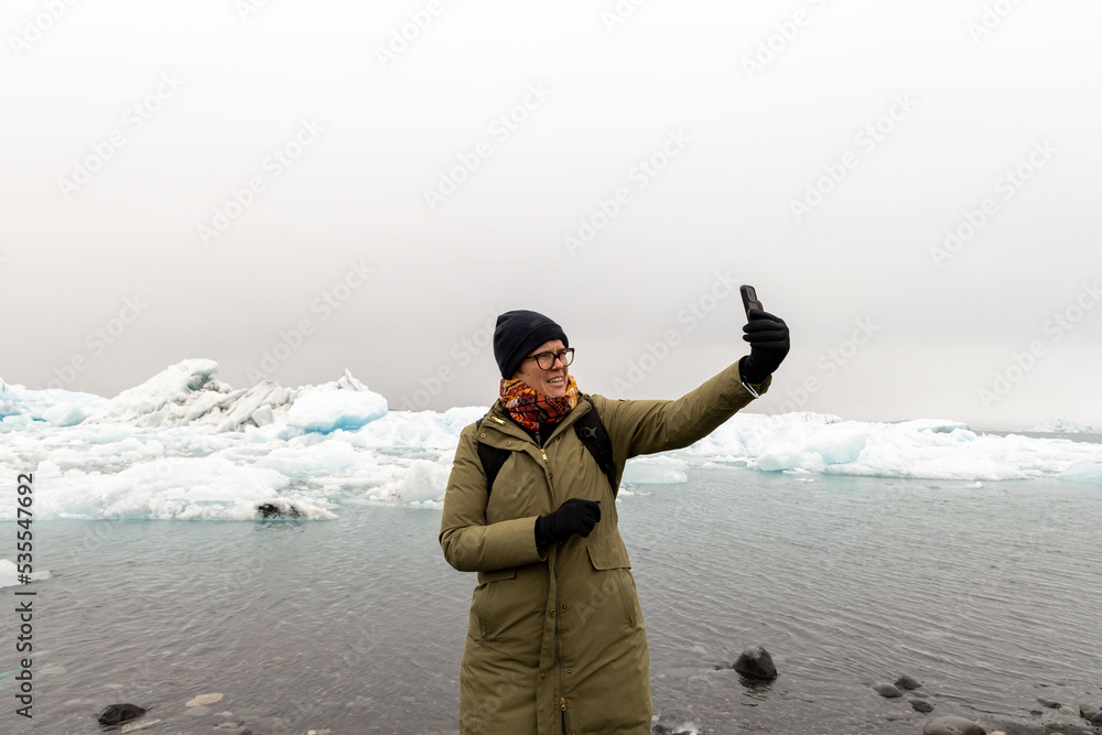 Caucasian woman taking a selfie with smartphone by the glacier in iceland Caucasian woman taking a selfie with smartphone by the glacier in iceland