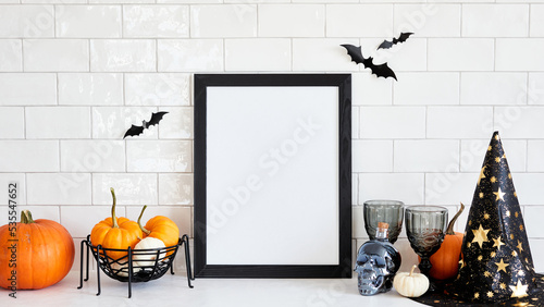Happy Halloween holiday concept. Picture frame mockup with witch hat, pumpkins, skull, wine glasses, bats on table in nordic home interior photo