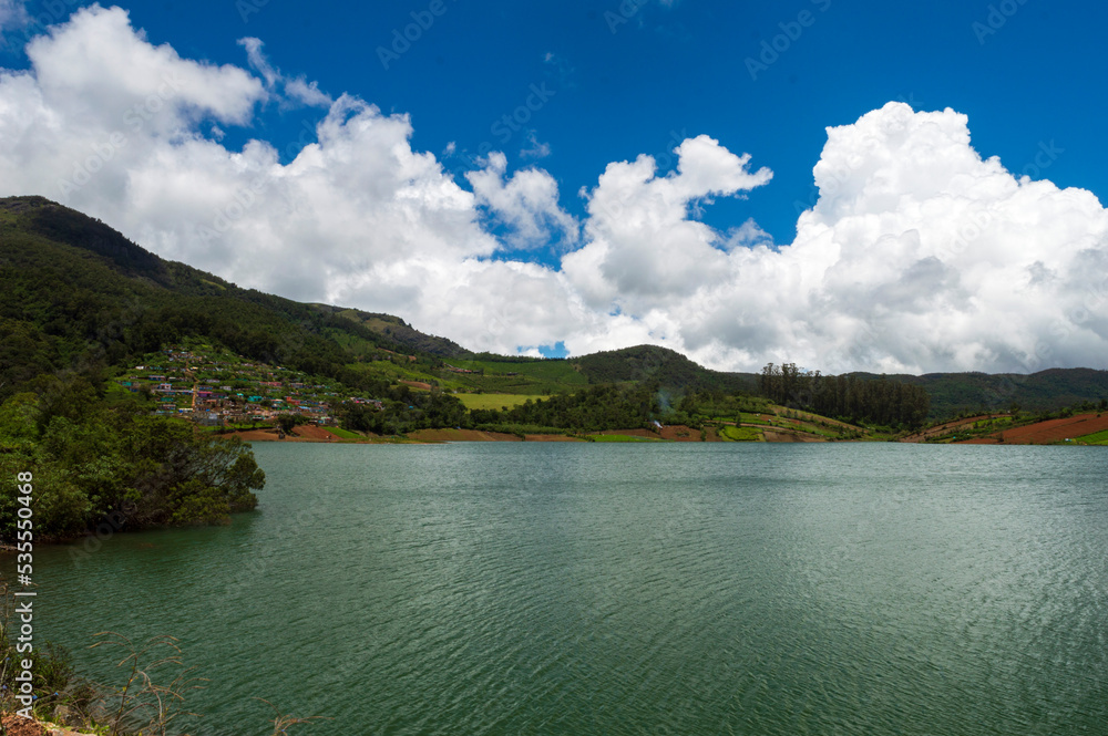 Scenic Ooty Lake, blue and white sky, reflection visible in water, nature's gift of greenery everywhere is the way one can explain the beauty of Ooty.