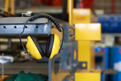 Yellow protective earmuffs hang on heavy industrial machines. This concept is a PPE device.