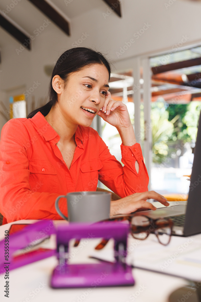 Happy biracial woman sitting at table in kitchen, using laptop Happy biracial woman sitting at table in kitchen, using laptop