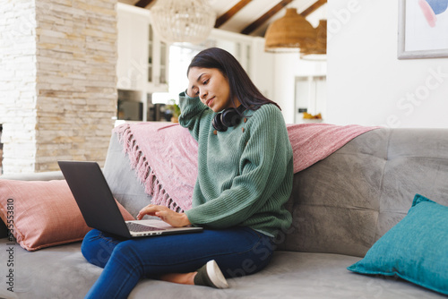 Happy biracial woman sitting on sofa in living room, using laptop photo