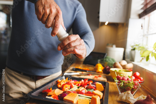 Midsection of caucasian man standing in kitchen and cooking dinner