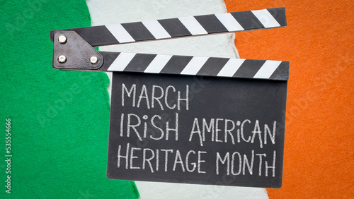 March Irish American Heritage Month, white chalk handwriting on a clapboard against paper abstract in colors of Ireland flag, reminder of annual monthly event
