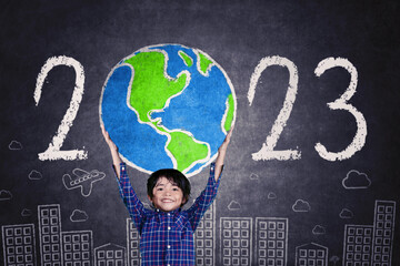 Little boy lifting a globe drawn with 2023 numbers