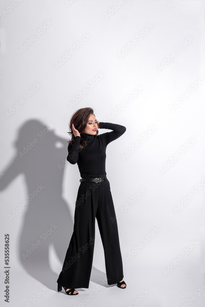 Fototapeta premium Beauty, fashion, style and make-up concept. Beautiful woman with dark pants and blouse studio portrait. Girl making various fashion poses. Model with long dark wavy hair, sun tan and red lipstick 