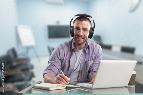 Young worker man with headphones at the table use laptop