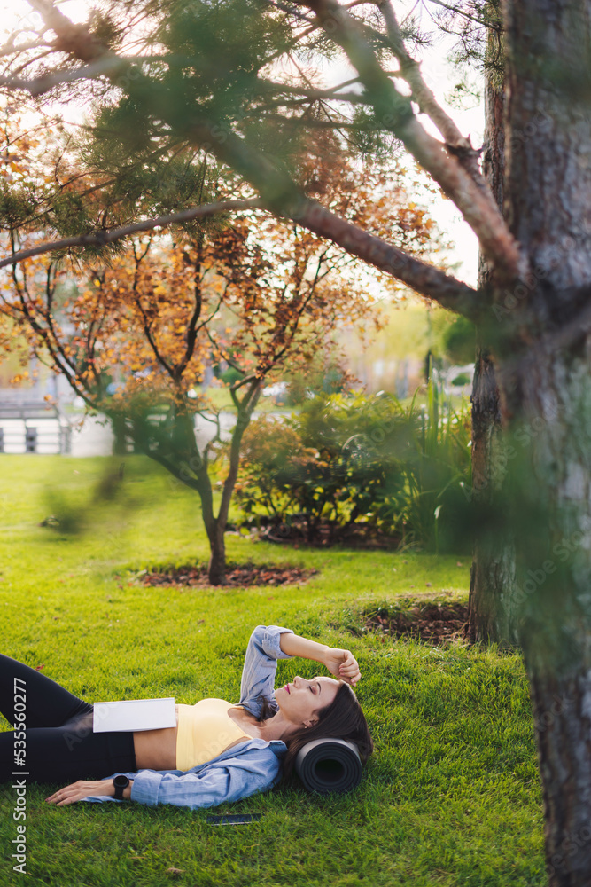 Beautiful woman in sportswear lying on the grass in the middle of a park fall asleep while reading a book. People lifestyle. Relax concept. Healthy lifestyle Beautiful woman in sportswear lying on the grass in the middle of a park fall asleep while reading a book. People lifestyle. Relax concept. Healthy lifestyle